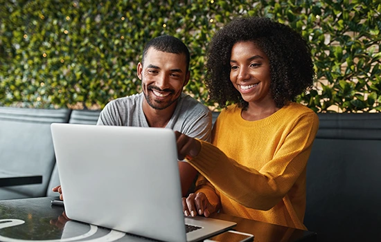 Two smiling professionals reviewing content together on a laptop in a modern office setting with green plant wall backdrop
